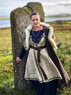 a woman dressed in medieval clothing standing next to a tree trunk with fur on it