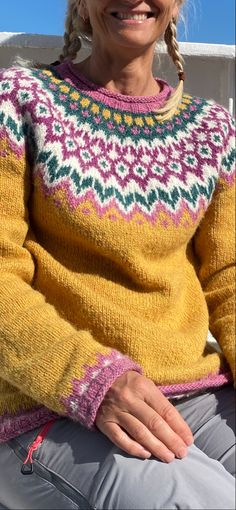 an older woman sitting on a bench wearing a yellow sweater and grey pants, smiling at the camera