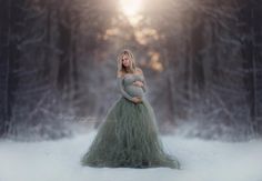 a pregnant woman is standing in the snow with her belly wrapped around her waist and wearing a long green dress