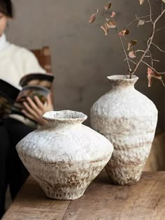 two white vases sitting on top of a wooden table next to each other with branches in them