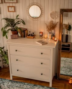 a white dresser with candles and plants on top