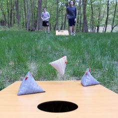 two people standing in the woods behind a wooden table with three triangular shaped objects on it