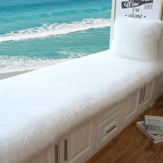 a white bench sitting on top of a hard wood floor next to the ocean in front of a window