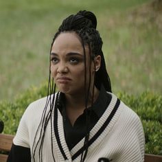 a woman with dreadlocks sitting on a bench looking at the camera while wearing a sweater