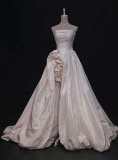 a white wedding dress on display in front of a black background with the back of it's skirt pulled up