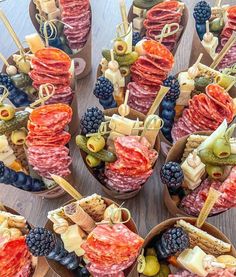 an assortment of meats and cheeses on skewers with fruit in bowls