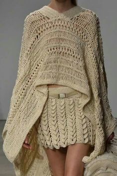 a model walks down the runway in a short skirt and knitted ponchy sweater