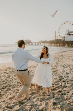 a man and woman holding hands on the beach near an amusement park ferris wheel in the background