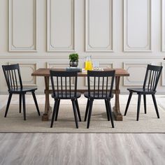 a dining room table with four chairs and a vase on top of it in front of a white wall