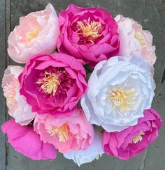 pink and white peonies are in a vase on the ground next to a brick wall