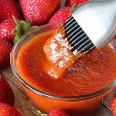 a spatula scooping tomato sauce out of a glass bowl filled with strawberries