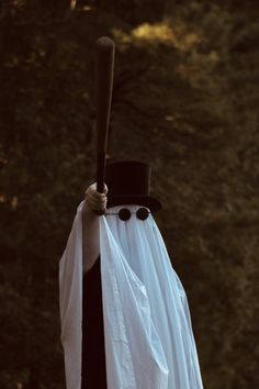 a person dressed up as a ghost holding a bat in their hand and wearing a top hat