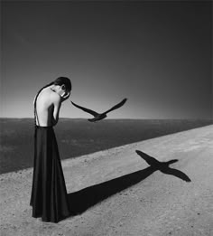 a woman standing on the side of a road with a bird flying over her head