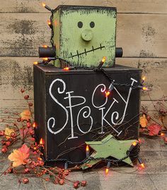 a wooden box with a green face on it sitting next to a string of lights