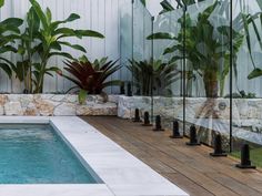 a pool surrounded by plants and rocks in a backyard with a wooden decking area