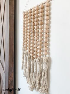 a wall hanging made out of wood beads and tassels on a white wall