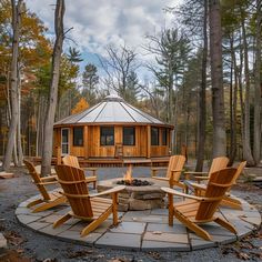 an outdoor fire pit surrounded by wooden chairs and tables in the woods with a gazebo behind it