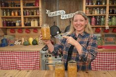 a woman holding up a jar filled with food in front of some jars on a table