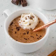 a cup of hot chocolate with whipped cream and chocolate pieces on the table next to it