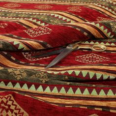 a pair of scissors are laying on a red and green patterned bed spread with gold trimmings