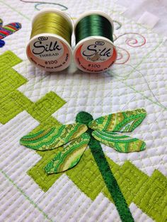 two spools of thread sitting on top of a quilted tablecloth with dragonfly applique