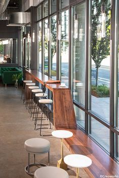 an empty restaurant with tables and stools in front of large windows that overlook the street