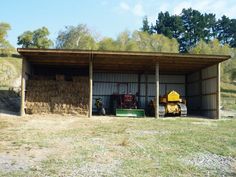 a shed with hay bales in the back and two tractors parked on the other side