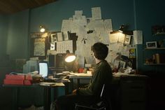 a person sitting at a desk in front of a computer monitor and lamp with papers all over it