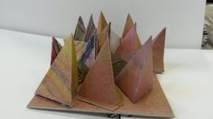 an origami sculpture is sitting on top of a white surface and it looks like three pyramids