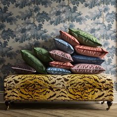 a pile of pillows sitting on top of a bench in front of a wallpapered wall