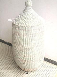 a large white basket sitting on top of a tiled floor next to a toilet paper dispenser