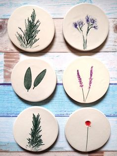 four coasters with pressed flowers and leaves on them, sitting on a wooden table