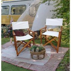 two wooden chairs sitting on top of a blanket in the grass next to a yellow van