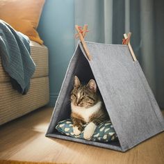 a cat is sitting in a teepee tent on the floor next to a pillow