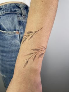 a woman's arm with a tattoo that has leaves on it and is next to her jeans