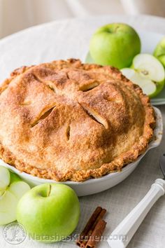 an apple pie sitting on top of a white plate next to apples and cinnamon sticks