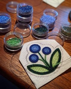 some beads are sitting on a table next to small bowls with blue and green beads