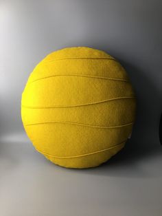 a yellow round pillow sitting on top of a gray floor next to a black chair