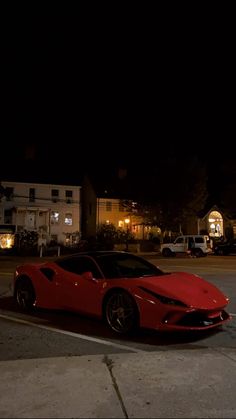 a red sports car parked in a parking lot at night with the headlights turned on