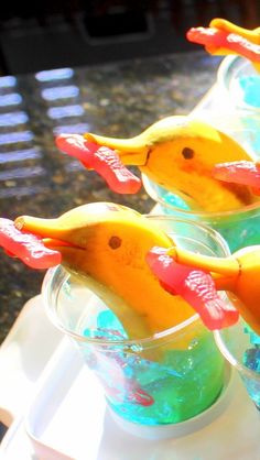 three plastic birds are sitting in cups filled with water and banana peels on a table