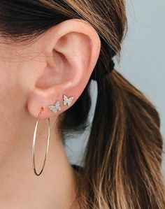 a woman wearing gold hoop earrings with small butterflies on the side of her ear,