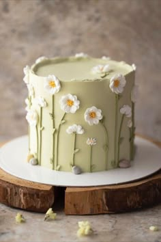 a green cake with white flowers on it sitting on a wooden plate next to a piece of wood