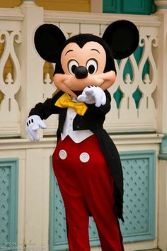 a mickey mouse mascot standing in front of a building wearing a suit and bow tie