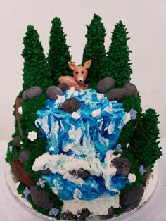 a cake decorated with trees and rocks has a deer sitting on it's head