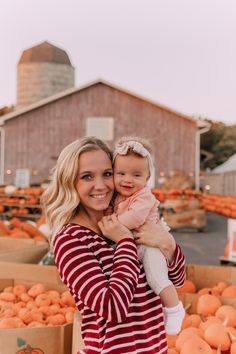 a woman holding a baby in front of pumpkins