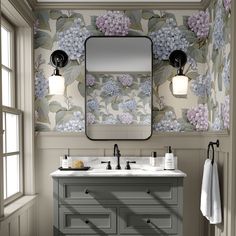 a bathroom vanity with two sinks and a large mirror above it, in front of a floral wallpaper