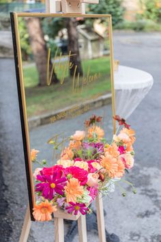 an easel with flowers on it sitting in front of a sign that says welcome to you