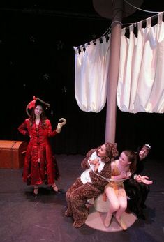 three people dressed in costumes on stage with one holding a teddy bear and the other sitting down