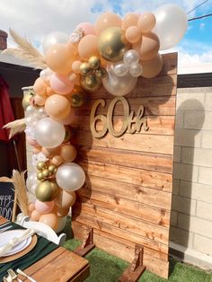 balloons are hanging from the side of a wooden sign that reads 60th with gold, white and peach colors