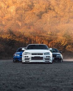 two cars are parked next to each other in front of some trees and bushes on a dirt road